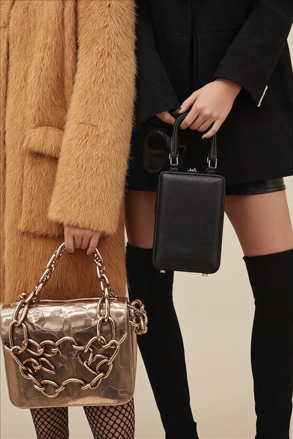 Dos personas mostrando bolsos de mano — uno dorado con cadenas, otro negro minimalista — fotografia de moda de cerca.